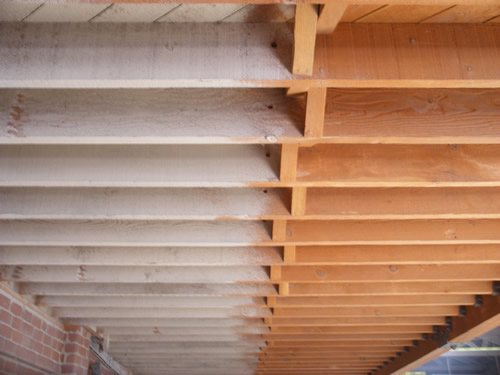 Vigas de madera a medio trabajo: a la izquierda con pintura, a la derecha ya limpias